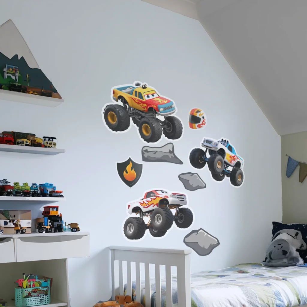 Väggdekor barn med monstertrucks uppsatta på en vit vägg i ett barnrum bredvid en säng och vita hyllor.